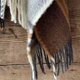 Klasiskas rūtis karameļi brūnos/pelēkos/baltos toņos indiāņu piegriezuma garais aitas vilnas pončo ar kapuci un bārkstīm